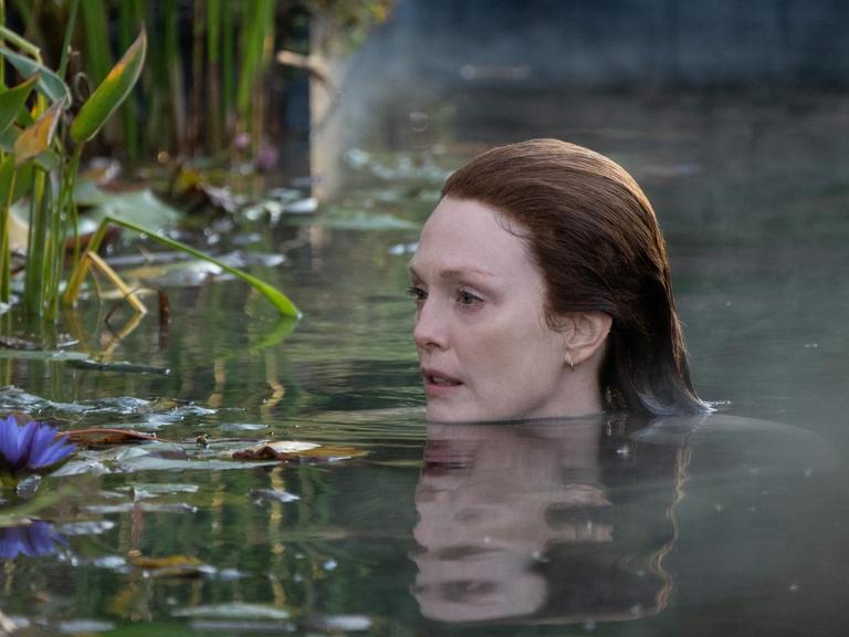 Die Schauspielerin Julianne Moore schwimmt im nebligen Wasser neben Schilf und Seerosen.