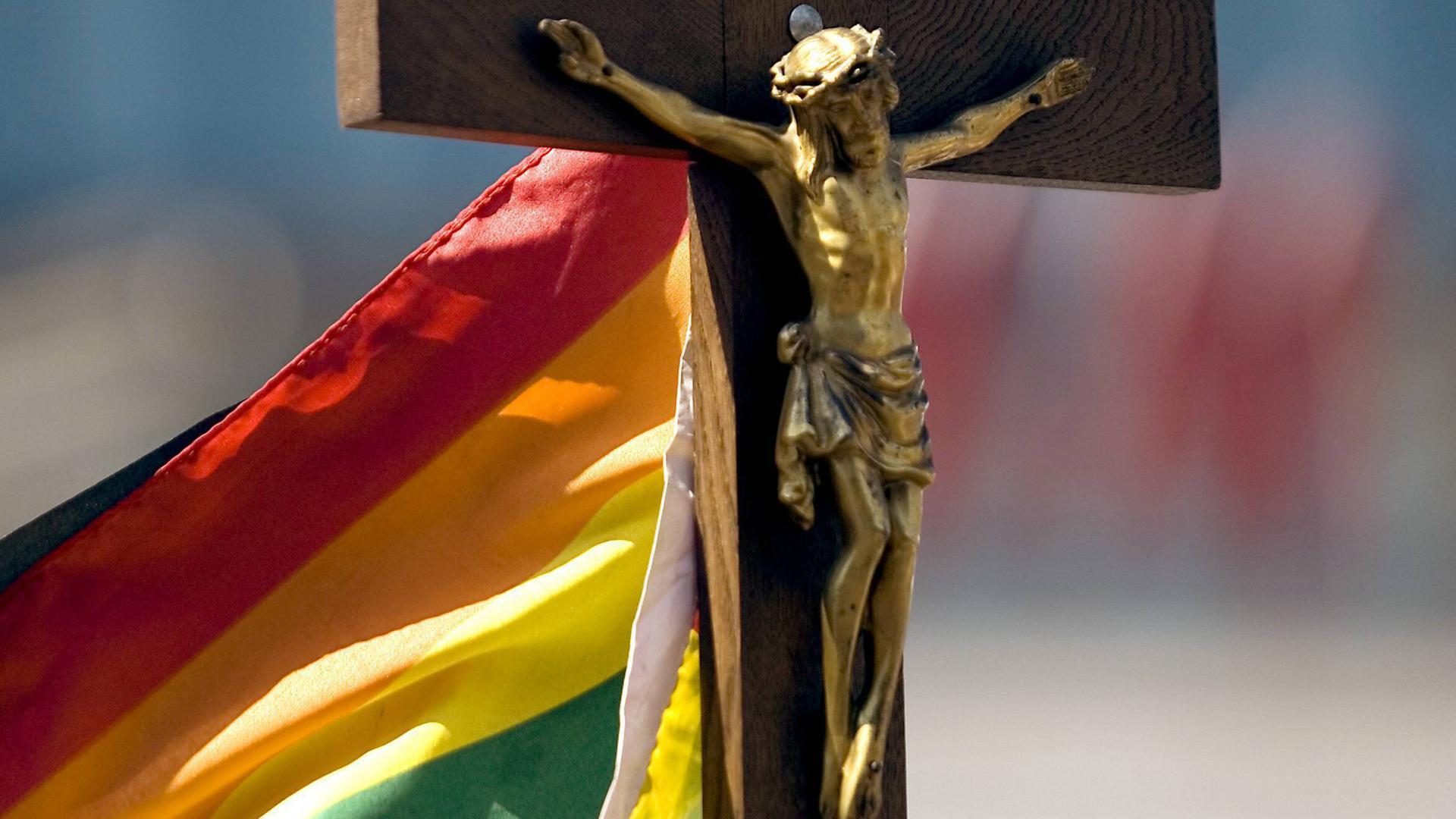 Das Bild zeigt eine Regenbogenflagge an einem Kruzifix.