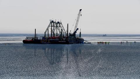 Das Endstück eines Seekabels wird von dem Kabelverlegeschiff "Boka Connector" im Watt unter dem Deich hindurch an Land gezogen.