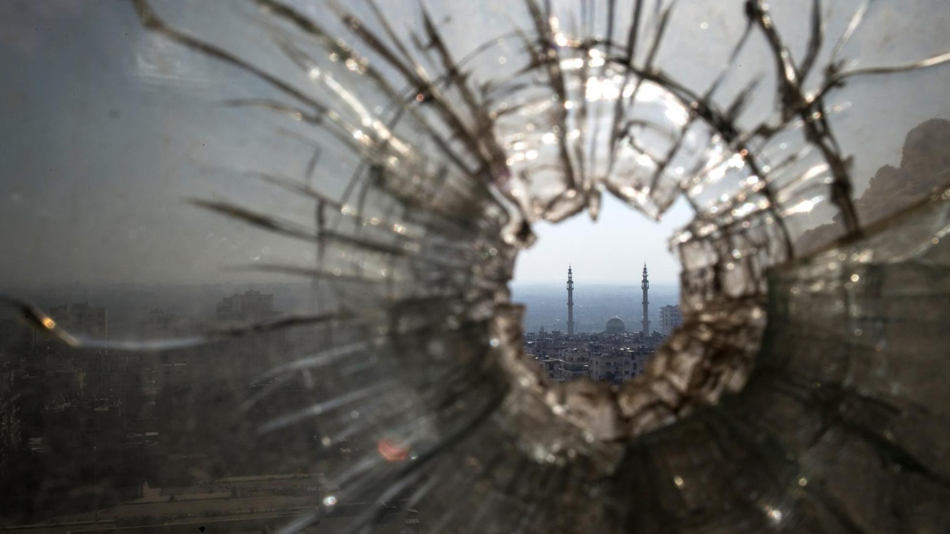 Blick durch ein zerschossenes Fenster auf eine Stadt in der arabischen Welt