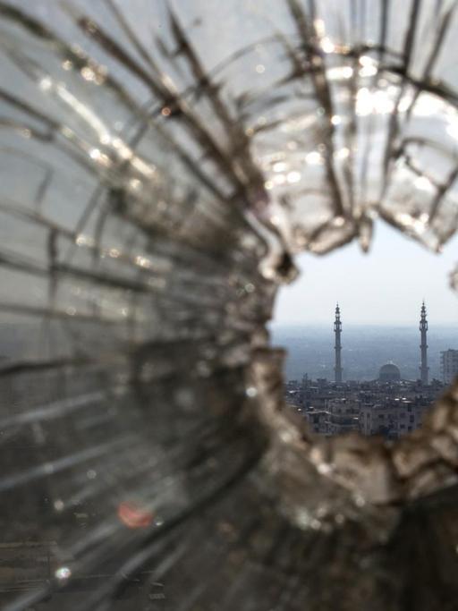 Blick durch ein zerschossenes Fenster auf eine Stadt in der arabischen Welt