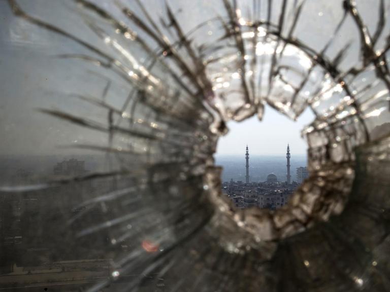 Blick durch ein zerschossenes Fenster auf eine Stadt in der arabischen Welt