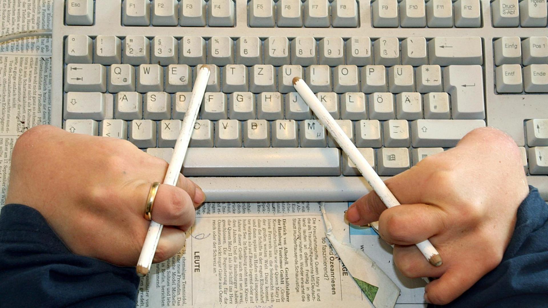 Ein Contergangeschädigter benutzt Radierstifte, um mit der Tastatur seines Computers zu arbeiten.