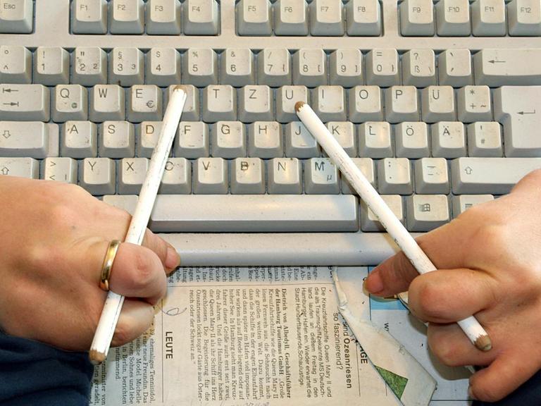 Ein Contergangeschädigter benutzt Radierstifte, um mit der Tastatur seines Computers zu arbeiten.