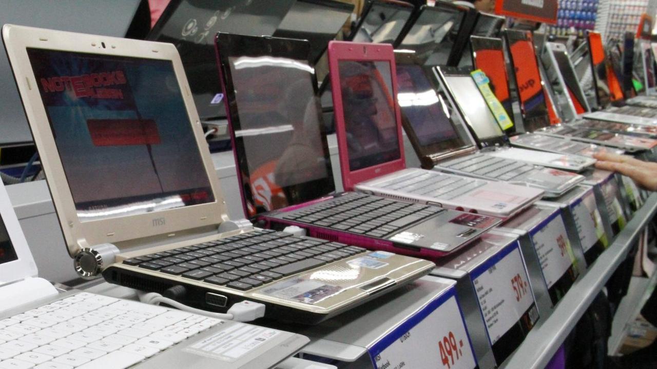 Notebooks und Laptops stehen nebeneinander aufgereiht auf einem Tisch in einem großen Elektonikmarkt. 