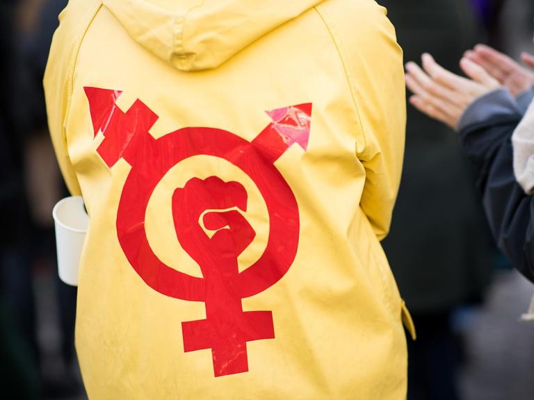 Eine Frau trägt einen gelben Regenmantel mit einem roten Gender- und Protestsymbol bei einer Kundgebung zum Internationalen Frauentag vor dem Rathaus in Hamburg.