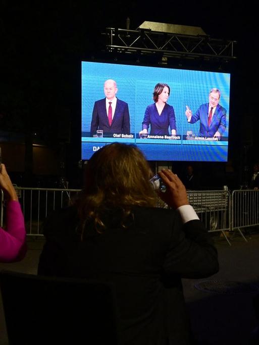 Zuschauerinnen filmen mit dem Smartphone eine Leinwand, auf der das TV-Triell der drei Kanzlerkandidaten übertragen wird.