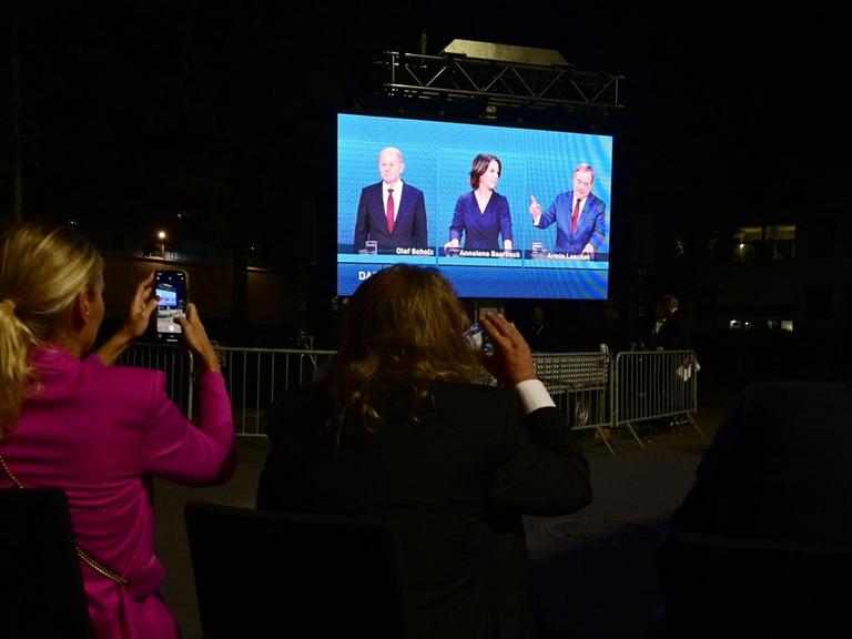 Zuschauerinnen filmen mit dem Smartphone eine Leinwand, auf der das TV-Triell der drei Kanzlerkandidaten übertragen wird.