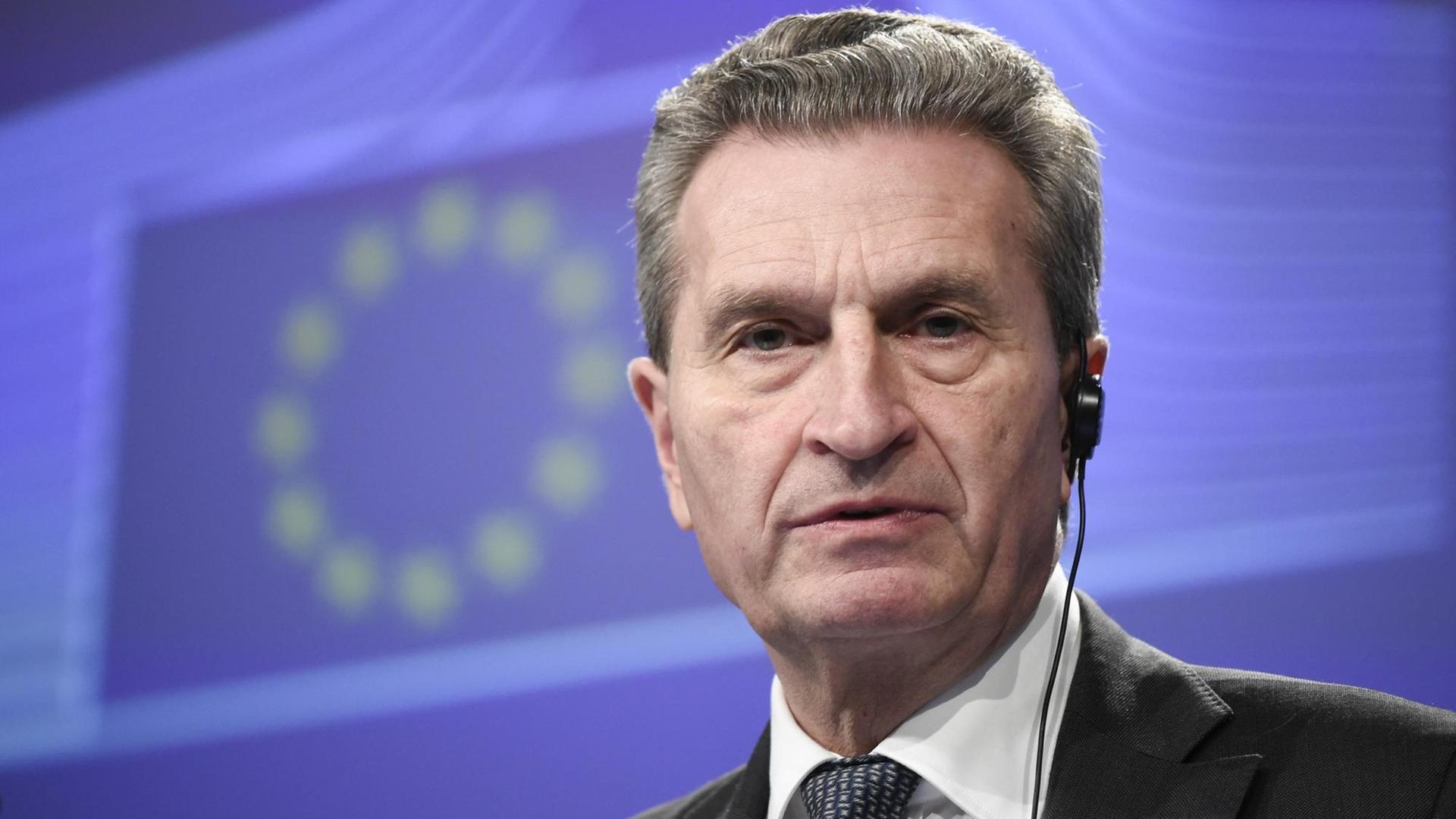 Oettinger steht vor einer blauen Wand mit den EU-Sternen.