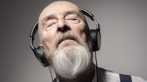 Ein alter Mann mit grauem Vollbart hört entspannt Musik mit Kopfhörern