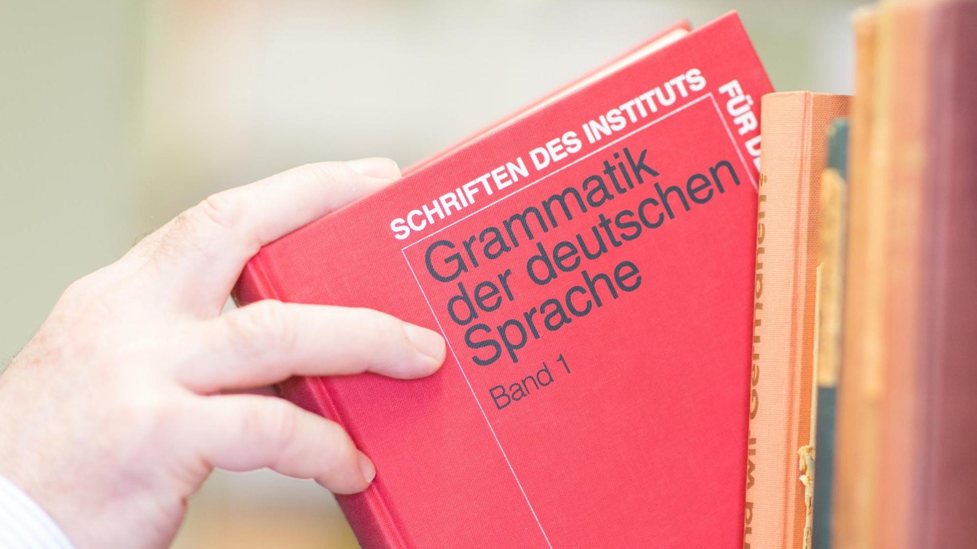 Ein Buch mit der Aufschrift "Grammatik der deutschen Sprache" wird aus einem Bücherregal genommen