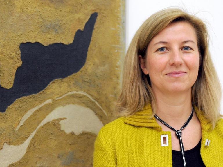 Ulrike Groos, Direktorin des Kunstmuseums in Stuttgart, steht mit Strickjacke vor einem abstraktem Bild.