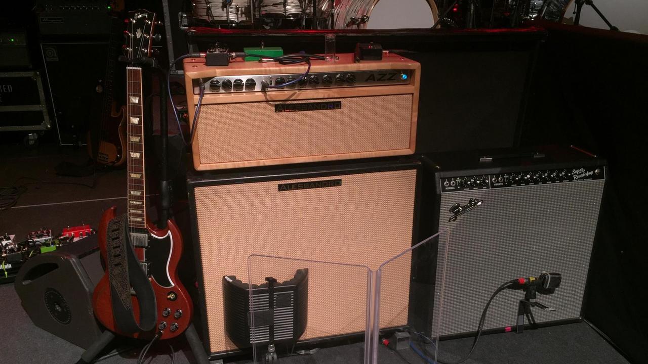 Eine rote Gitarre steht auf einer Konzertbühne neben zwei Gitarrenverstärkern.