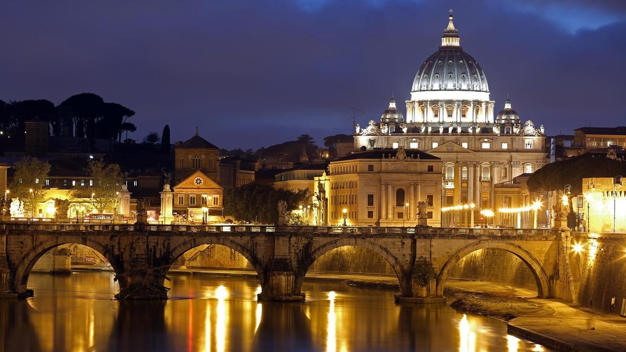 Der Petersdom im Vatikan vor dem abendlichen Himmel. Vorne verläuft die Engelsbrücke über den Tiber.
