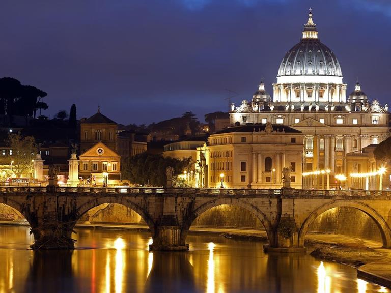 Der Petersdom im Vatikan vor dem abendlichen Himmel. Vorne verläuft die Engelsbrücke über den Tiber.