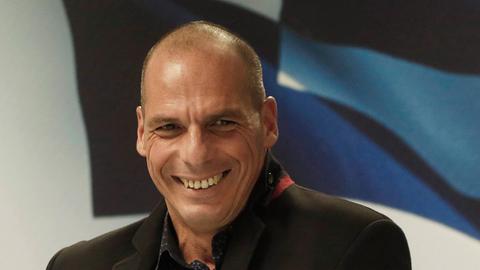 Yanis Varoufakis steckt lachend ein Blatt Papier in die Innentasche seiner Jacke.