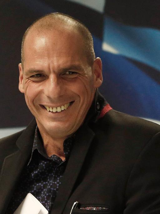 Yanis Varoufakis steckt lachend ein Blatt Papier in die Innentasche seiner Jacke.