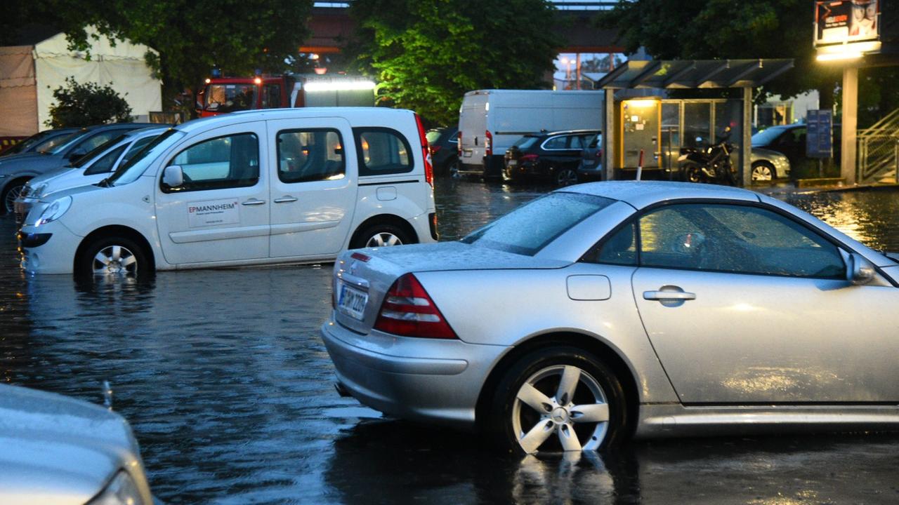 Nach einem schweren Gewitter mit Starkregen stehen Autos in Manheim auf einem teilweise überflutetem Parkplatz.