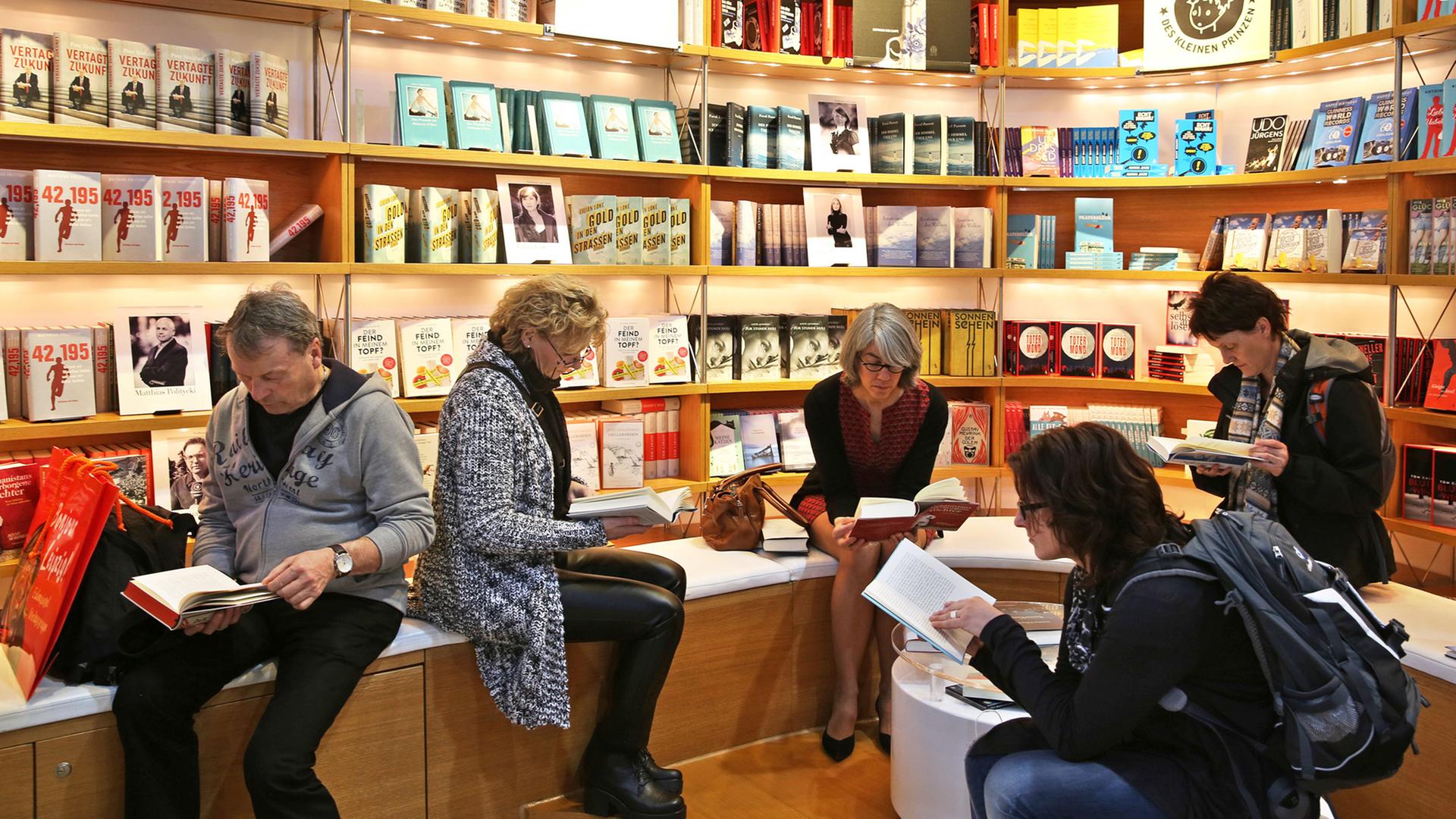 Vier Frauen und ein Mann sitzen vor einer Bücherwand und lesen.