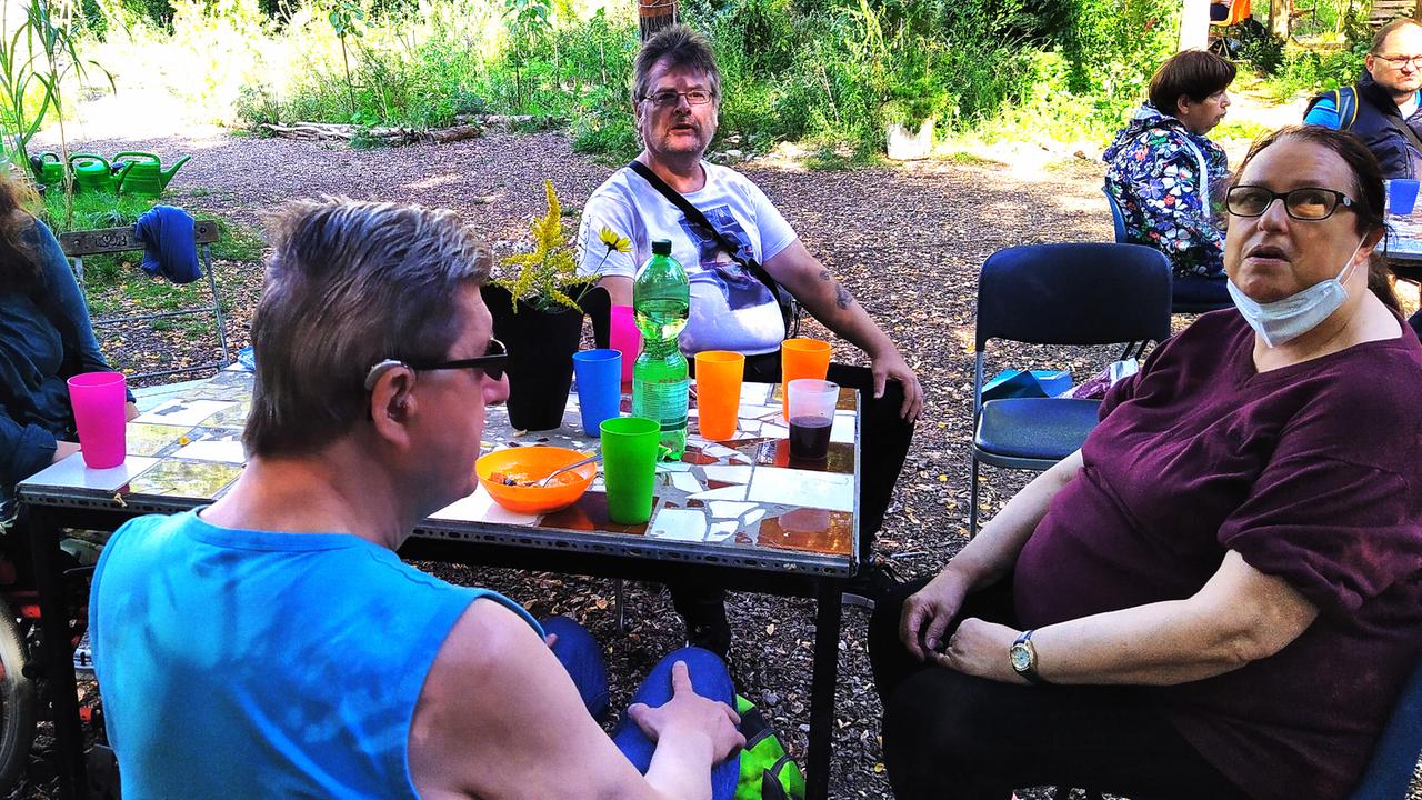Menschen mit Behinderung sitzen um Tische in einem Garten