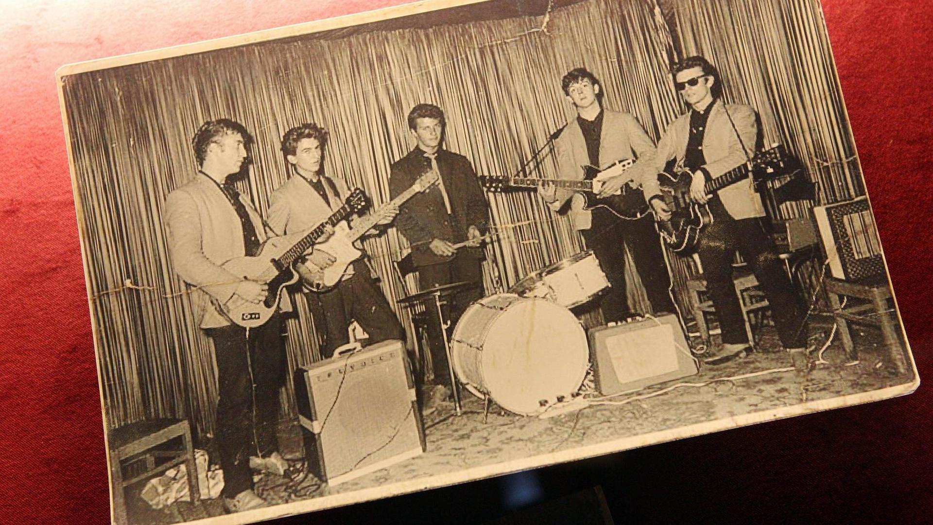 Eine Schwarzweißfotografie auf Papier zeigt die Beatles bei ihrem ersten Auftritt im Hamburger Indra-Club am 17. August 1960.