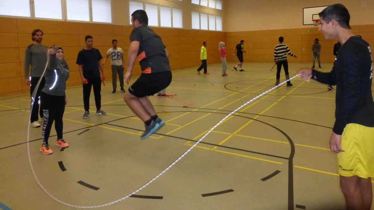In einer Berliner Sporthalle werden Flüchtlinge als Sporttrainer ausgebildet. Auf dem Foto springt ein junger Mann über ein Seil.