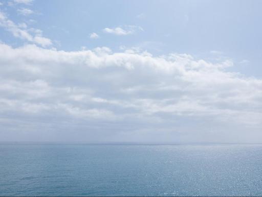 Meer mit blauem Himmel und weißen Wolken am Horizont.