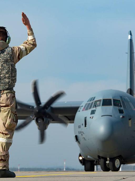 Ein Soldat steht auf dem Rollfeld der US Air Base Ramstein und gibt einem C-1301J Super Hercules Transportflugzeug Kommandos.