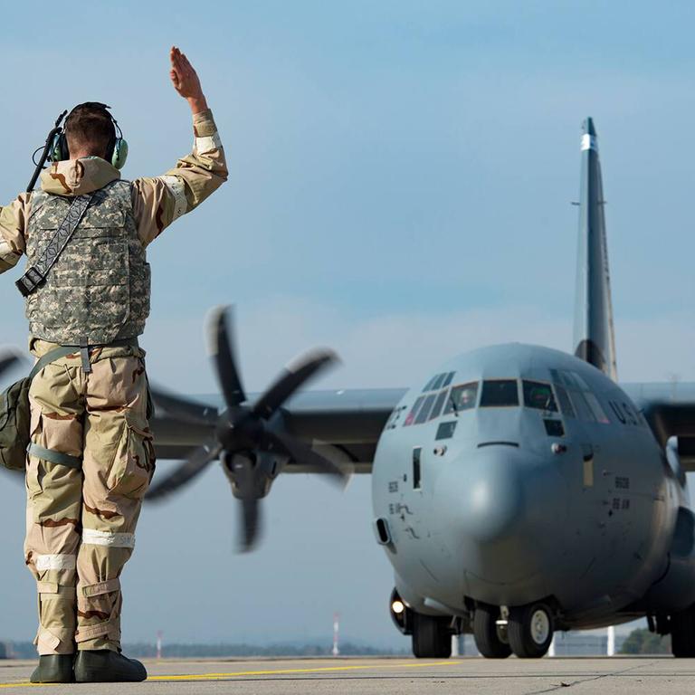 Ein Soldat steht auf dem Rollfeld der US Air Base Ramstein und gibt einem C-1301J Super Hercules Transportflugzeug Kommandos. 