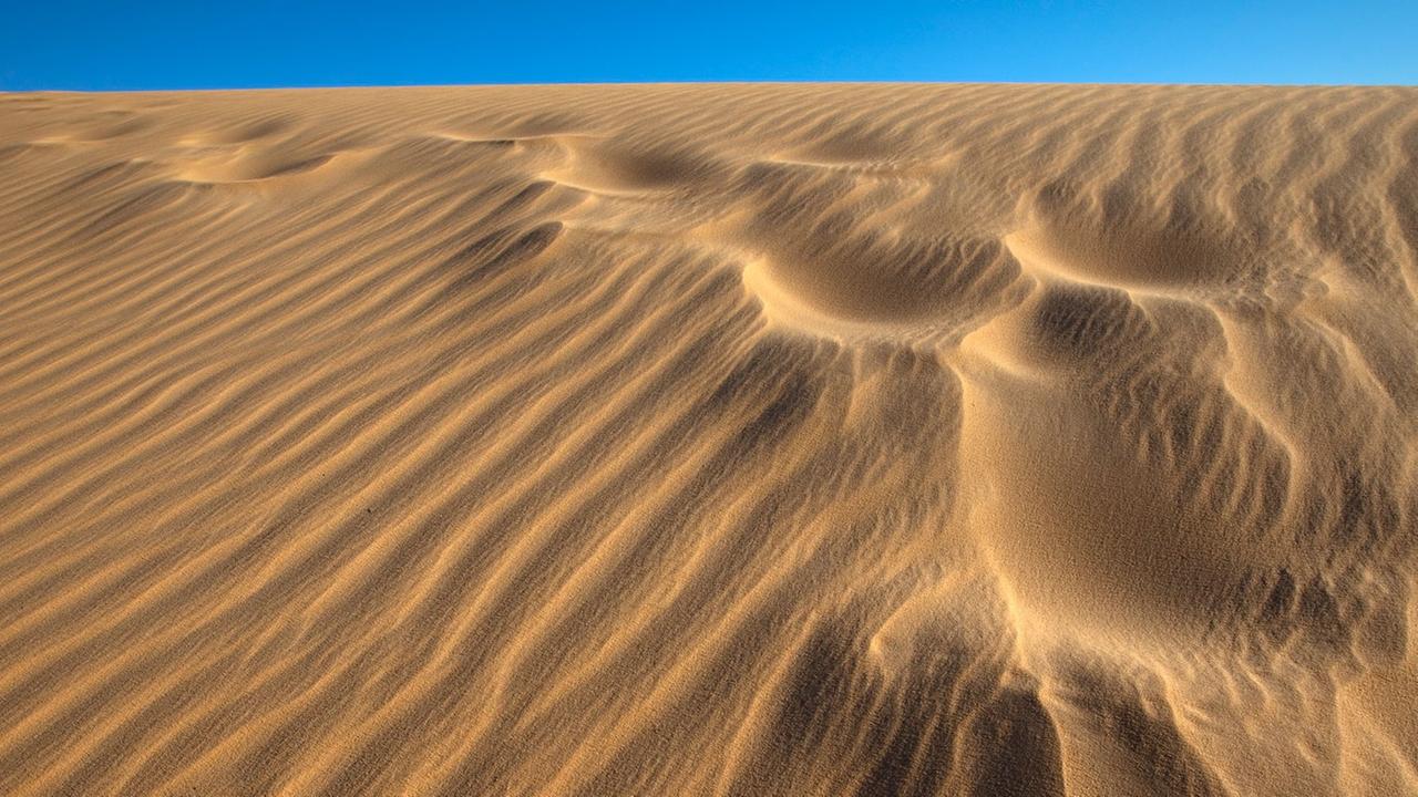 Verwehte Fußspuren auf einer Sanddüne bei Assuan in Ägypten, im Hintergrund blauer Himmel