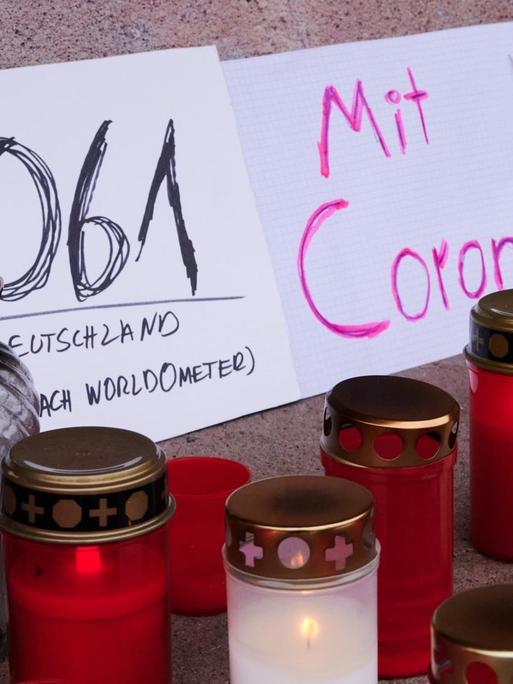 Mehrere Plakate, Grablichter und Kerzen stehen auf dem Podest des Stierbrunnens in Prenzlauer Berg und erinnern an die die aktuelle Zahl der Toten durch Corona in Deutschland. (Januar 2021)