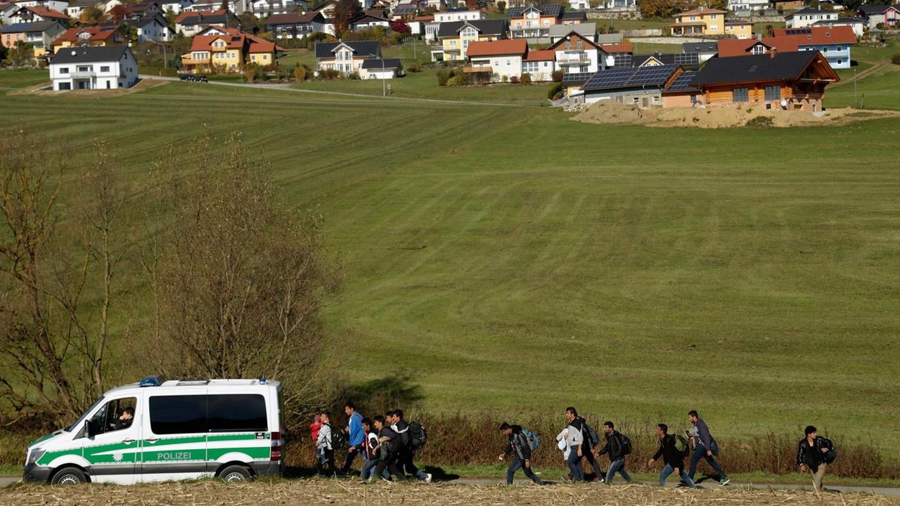 Ein Polizeiwagen und eine Gruppe von Migranten auf einem Feld vor einem bayrischen Dorf.