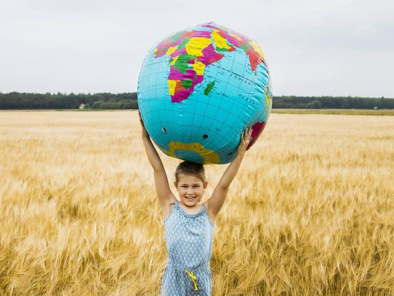 Ein Mädchen steht mit einer großen Weltkugel als Ball in einem Kornfeld.