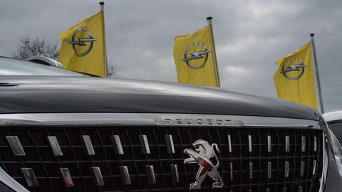 Opelfahnen wehen hinter einem Auto von Peugeot durch die Luft bei einem Autohaus in Darmstadt.