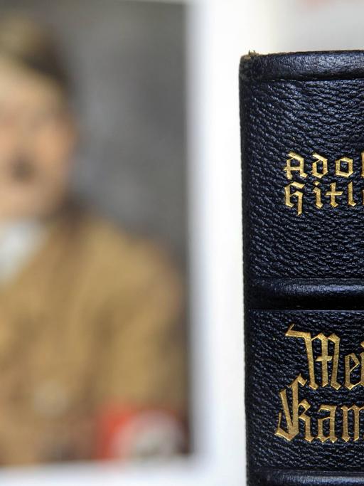 Der Buchrücken einer Ausgabe von Hitlers "Mein Kampf" vor einem unscharfen Porträtbild Hitlers.