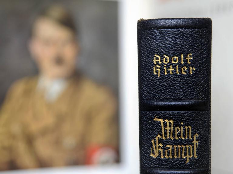 Der Buchrücken einer Ausgabe von Hitlers "Mein Kampf" vor einem unscharfen Porträtbild Hitlers.