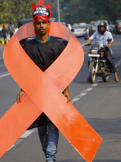 Ein Aktivist trägt ein Aids-Logo um den Körper, das etwa genauso groß ist wie er. Er geht auf einer Straße in Bhubaneswar in Indien.