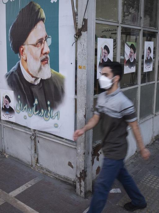 Ein Mann läuft an der Fassade eines Geschäfts vorbei, die mit Wahlplakaten von Ebrahim Raisi beklebt ist.