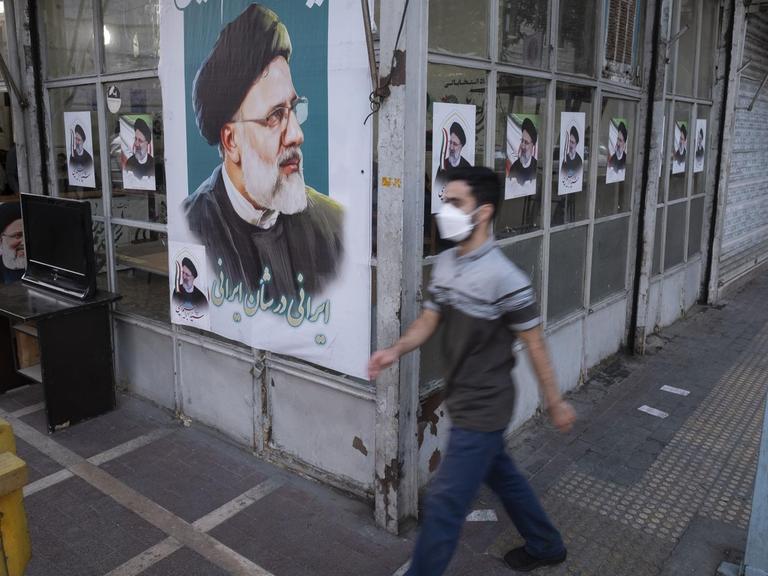 Ein Mann läuft an der Fassade eines Geschäfts vorbei, die mit Wahlplakaten von Ebrahim Raisi beklebt ist.
