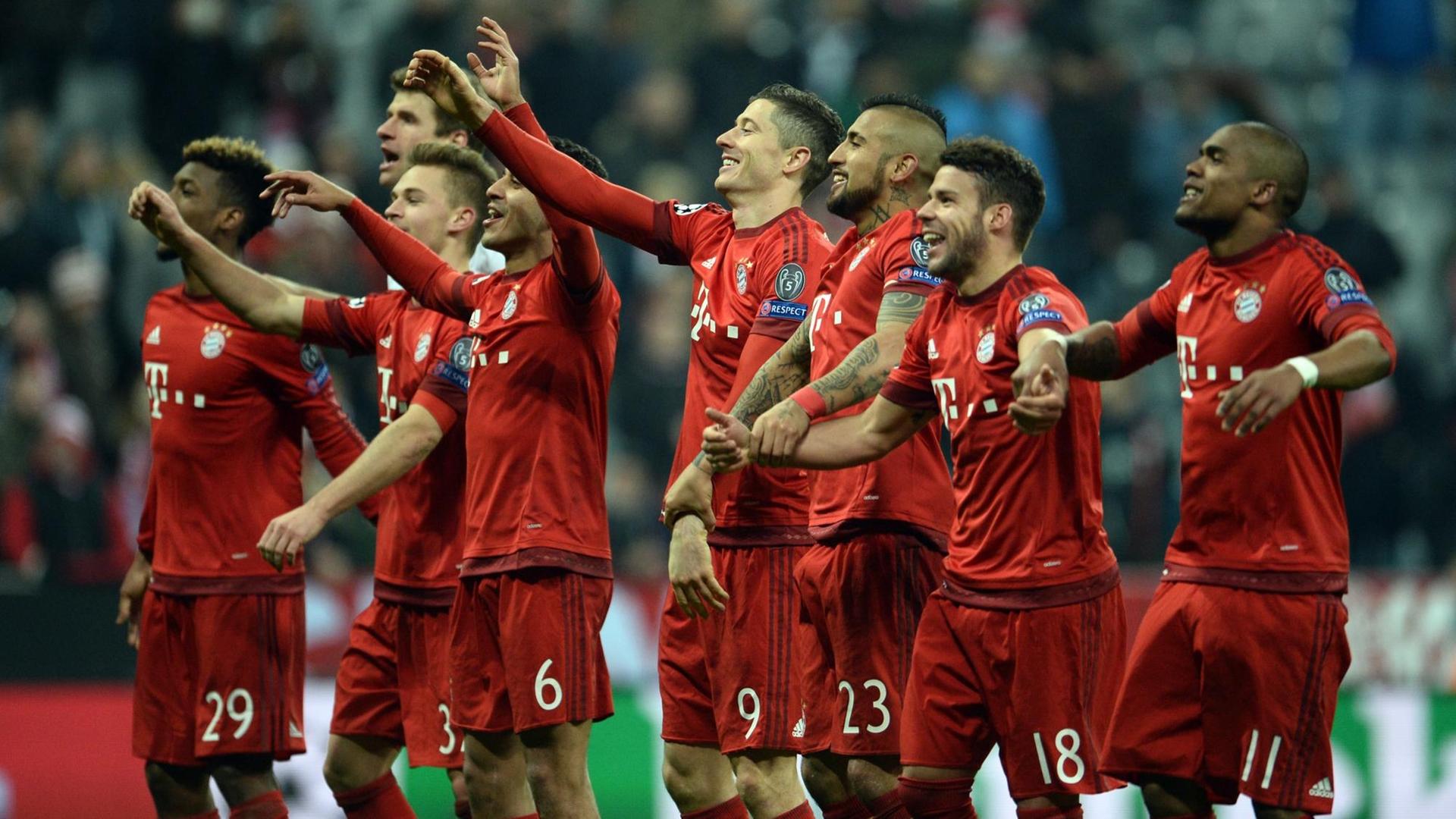 Man sieht die Spieler des FC Bayern in roten Trikots, sie jubeln und heben dabei die Arme.