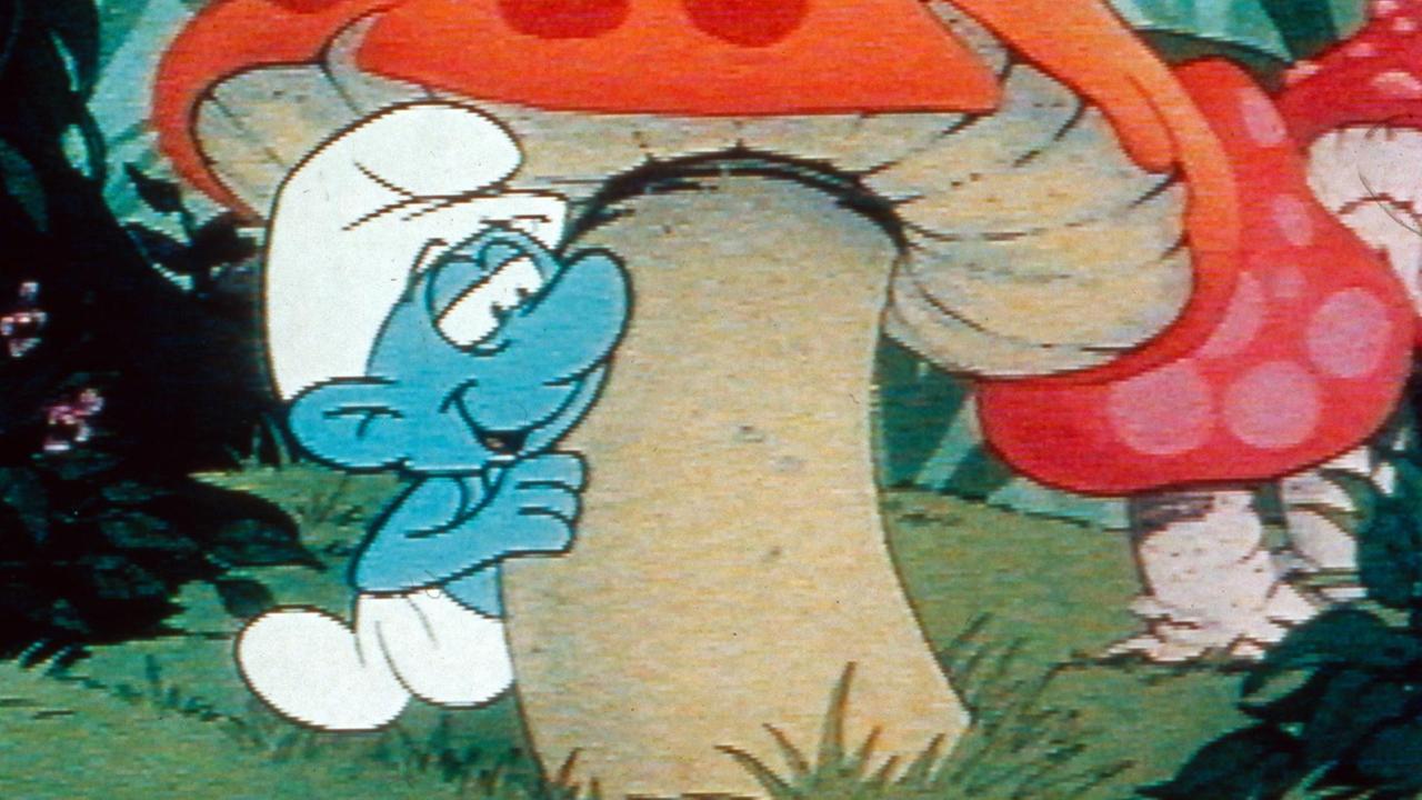 Ein Schlumpf schaut hinter einem Fliegenpilz hervor. Szene aus einer Zeichentrickserie (1981)