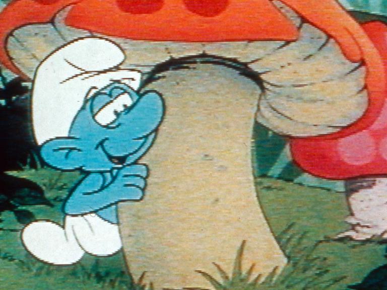Ein Schlumpf schaut hinter einem Fliegenpilz hervor. Szene aus einer Zeichentrickserie (1981)