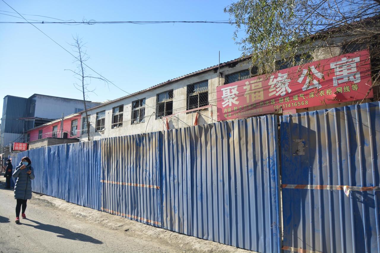 Ein ausgebranntes Appartementhaus in Peking wird von einem blauen Bauzaun gesichert.