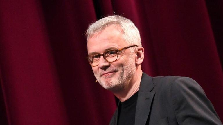Christoph Terhechte steht auf der Bühne. Er trägt ein schwarzes Sakko und schaut freundlich in das Publikum. Christoph Terhechte steht auf der Bühne. Er trägt ein schwarzes Sakko und schaut freundlich in das Publikum.