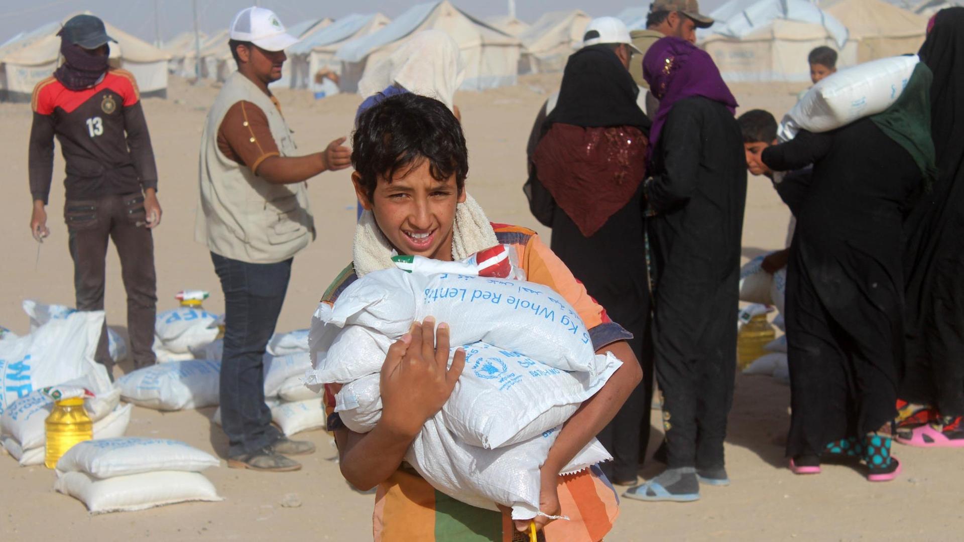 Ein irakisches Flüchtlingskind in der eingeschlossenen Stadt Falludscha trägt einen Sack mit Lebensmitteln, der von der WFP gespendet wurde.