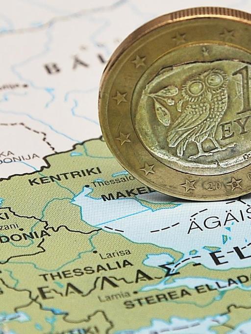 Eine griechische Euro-Münze steht hochkant auf einer Landkarte Griechenlands.