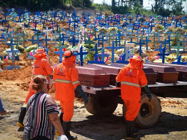 Brasilien, Manaus: Friedhofsmitarbeiter, gefolgt von Angehörigen der Toten mit Mundschutzmasken, fahren Särge zu einem Massengrab. Angesichts der steigenden Zahl von Corona-Infektionen ist das Gesundheitswesen in Manaus am Limit.