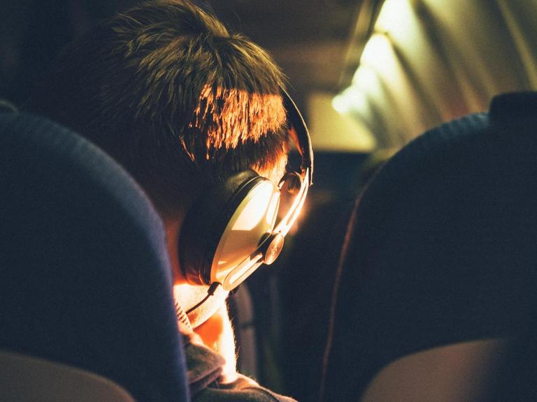 Das Bild zeigt den Hinterkopf eines Menschen mit Kopfhörern in einem Zugabteil, der bestimmt Podcasts hört.