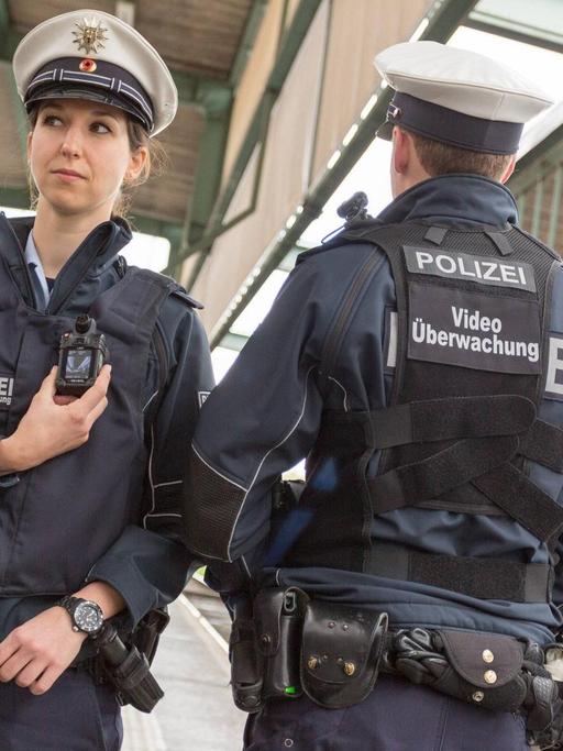 Zwei Polizisten präsentieren die neuen Bodycams: mit einem Monitor auf der Brust, einer Kamera auf der Schulter und dem Schriftzug "Videoüberwachung" auf dem Rücken