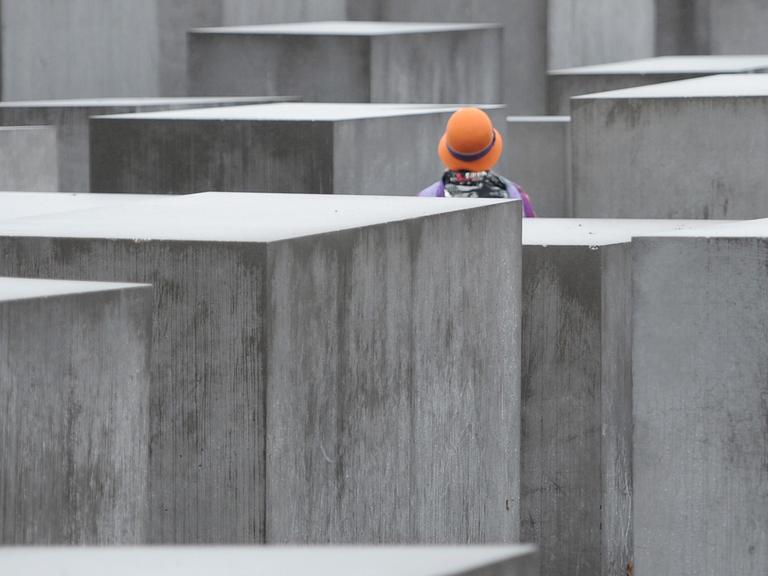Eine Frau mit buntem Hut steht am 09.12.2013 in Berlin im Nieselregen zwischen den Stelen des Holocaust-Mahnmals in Berlin.